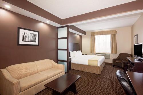a hotel room with a bed and a couch and a tv at Ramada by Wyndham Cold Lake in Cold Lake