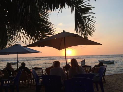 a group of people sitting on the beach watching the sunset at Paradise Bay in Beruwala