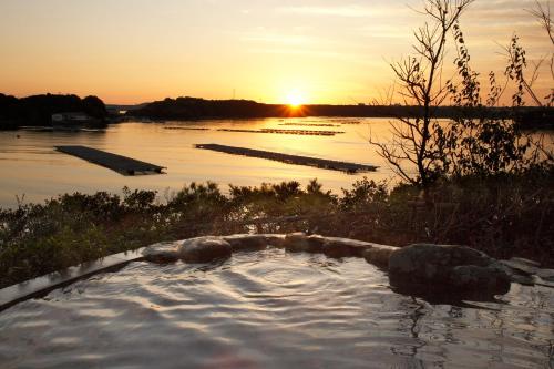 a hot tub in the middle of a river at sunset at Kashikojima Hojoen in Shima
