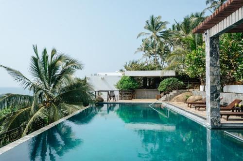 a swimming pool with blue water and palm trees at Rumassala Villas in Unawatuna