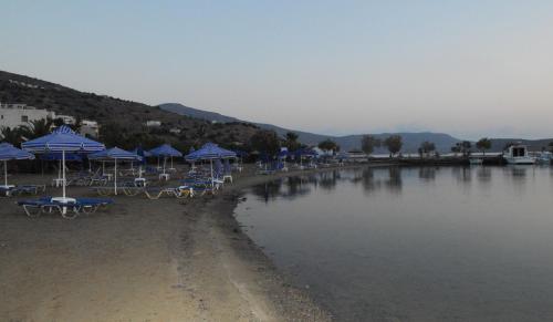 a beach with blue umbrellas and chairs next to the water at Palemilos Apartments in Elounda