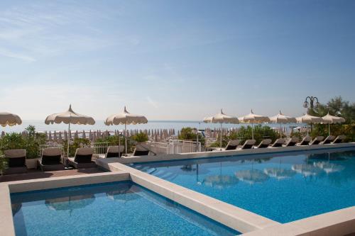 einen Pool mit Stühlen und Sonnenschirmen sowie das Meer in der Unterkunft Hotel Delle Nazioni in Lido di Jesolo