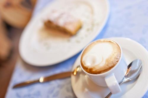 a cup of coffee on a plate with a piece of cake at Brunnerhof Klausen-Chiusa in Chiusa
