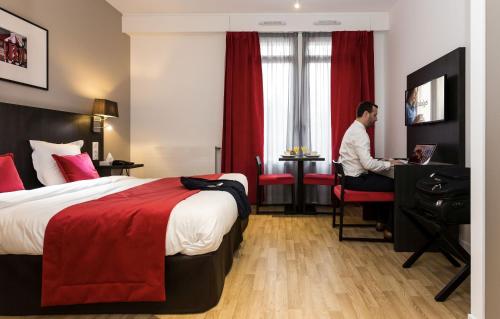 um homem sentado numa secretária num quarto de hotel em Odalys City Paris Montmartre em Paris