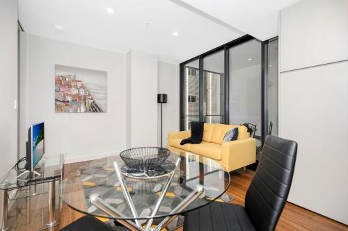 a living room with a glass table and a yellow chair at Astra Apartments Newcastle Beach in Newcastle