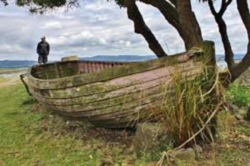 a man standing next to a wooden boat on a field at Noah's Boutique Accommodation Moeraki in Moeraki