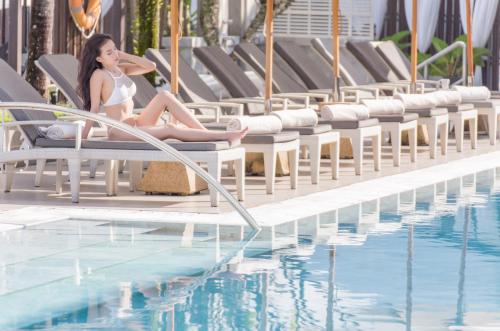 a woman in a white bikini sitting next to a swimming pool at Cape Sienna Phuket Gourmet Hotel & Villas - SHA Extra Plus in Kamala Beach
