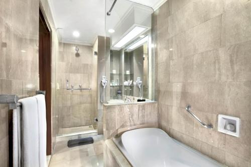 a bathroom with a tub and a shower and a sink at ASTON Tropicana Hotel Bandung in Bandung