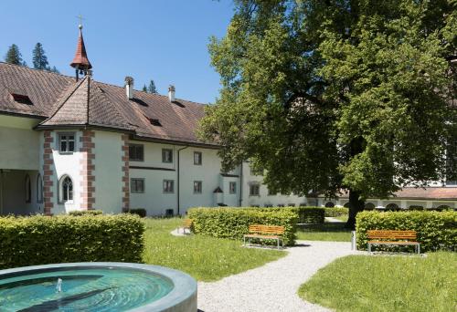 a building with a swimming pool in a yard with two benches at Hotel Kloster Fischingen in Fischingen