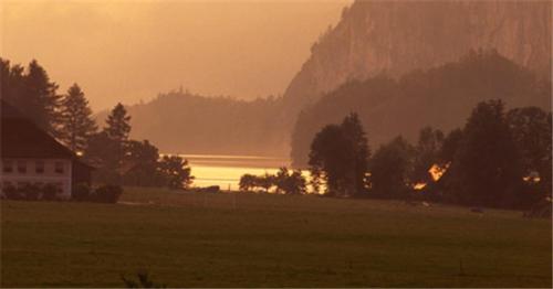 a sunset over a field with a house and a mountain at Seehotel Huber in Sankt Gilgen
