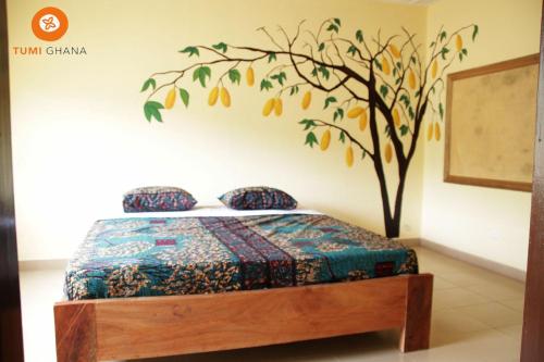 a bedroom with a bed with a tree painted on the wall at Tumi Hostel in Kumasi