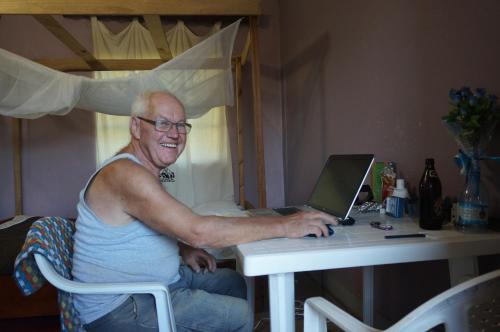an older man sitting at a desk with a laptop computer at Masaka Backpackers, Tourists Cottage & Campsite in Masaka