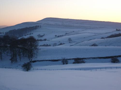a snow covered field with a fence in the foreground at The Lantern Pike Inn in Hayfield