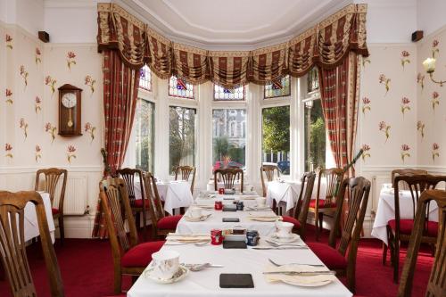 uma sala de jantar com mesas, cadeiras e janelas em Lincoln House Private Hotel em Cardiff