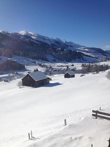 a snow covered field with a barn and mountains at Zimmer & z'Morgä Schönenboden in Wildhaus