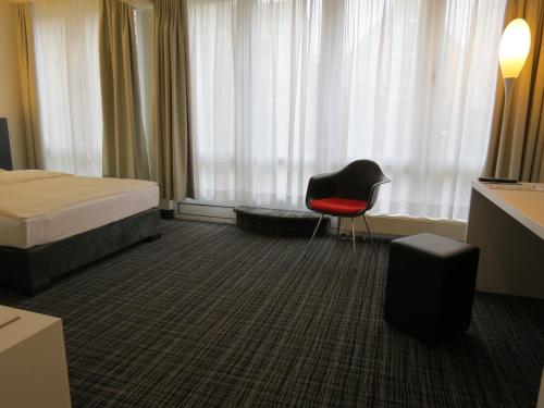 a bedroom with a bed and a chair in front of a window at Comfor Hotel Ulm City in Ulm