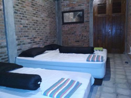 three beds in a room with a brick wall at Rumah Limas in Yogyakarta