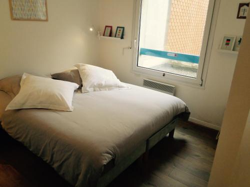 a bed with white sheets and pillows in a room with a window at les pieds dans l'eau in Wimereux