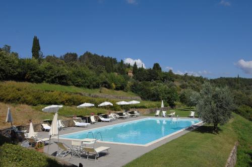 a swimming pool with chairs and umbrellas next to a hill at Castello Di Gargonza in Monte San Savino