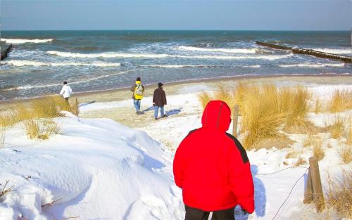a person in a red jacket walking on the beach at Am Weststrand Aparthotel Kühlungsborn in Kühlungsborn