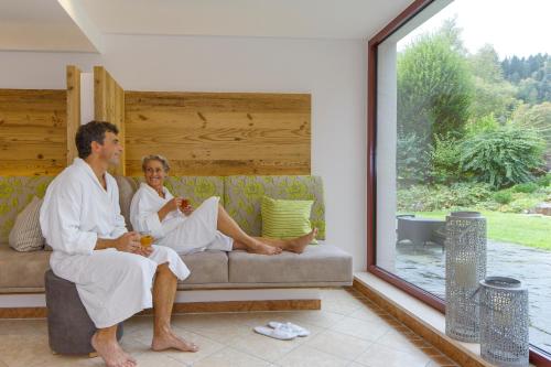 a man and woman sitting on a couch in a living room at Hotel Thomahof in Hinterzarten