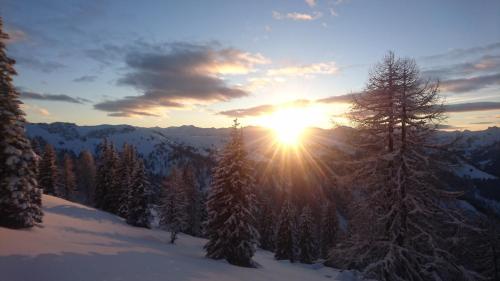 a sun setting over a snow covered mountain with trees at Appartementhaus Unterkofler in Grossarl