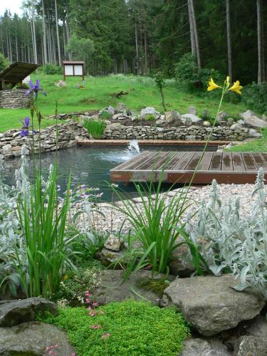 a garden with a pond with a bridge and flowers at Penzion Na Habeši in Kašperské Hory