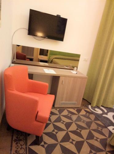 an orange chair sitting in front of a desk with a television at Hotel Etnea Royal Suites in Catania