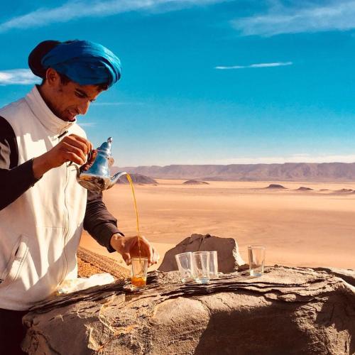 a man pouring a drink into a table in the desert at Riad Les Jardins de Tafraoute in Foum Mharech