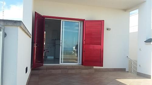 a red pivot door on a white building with a glass door at Monolocale sul Lungomare San Foca in San Foca