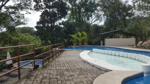 a swimming pool with a brick walkway next to a resort at Villa privada con Jacuzzi Herradura Jaco in Herradura