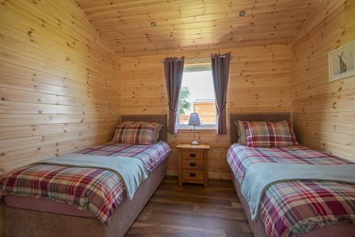 two beds in a log cabin with a window at The Chalet, Holidays for All in Dunbar