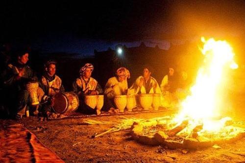 a group of people sitting around a fire at night at Camp Sahara Holidays in Mhamid