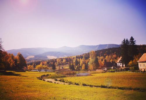 a grassy field with a river and mountains in the background at Drewniana Róża Domki Karkonosze in Piechowice