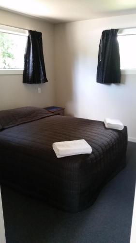 a bedroom with a bed with black sheets and two windows at Fairlie Holiday Park in Fairlie