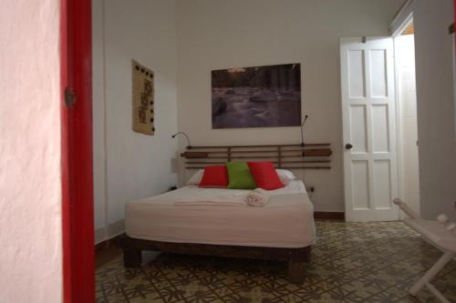a small bedroom with a bed with a red and green pillow at La Puerta Roja Guest House in Santo Domingo
