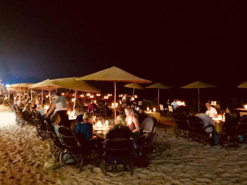 un grupo de personas sentadas en las mesas de la playa por la noche en Sealand Beach Cottages, en Patnem