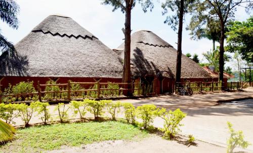 two thatched huts with trees and a fence at The Palms Beach Hotel and Restaurant Limited in Entebbe