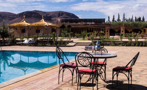 una mesa y sillas sentadas frente a una piscina en Dar Alfourssane Ferme d’hôte, en Ouarzazate