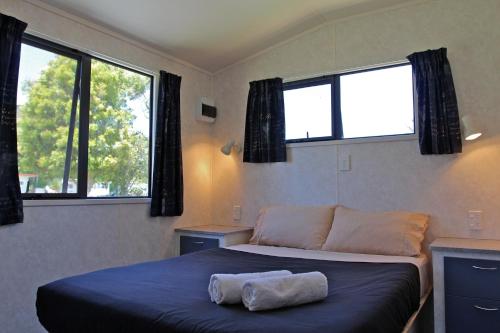 a small bedroom with a bed with two windows at Russell-Orongo Bay Holiday Park in Russell