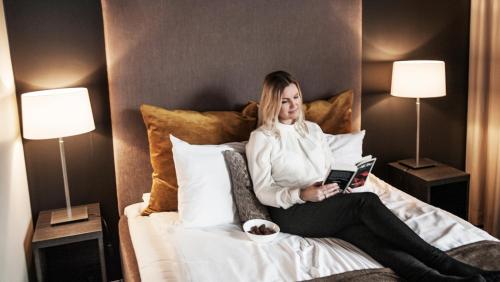 a woman sitting on a bed reading a book at Wilhelmsen House in Tønsberg