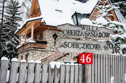 a wooden sign in front of a house with a fence at Rezydencja Sąsiadów Zakopanego in Zakopane