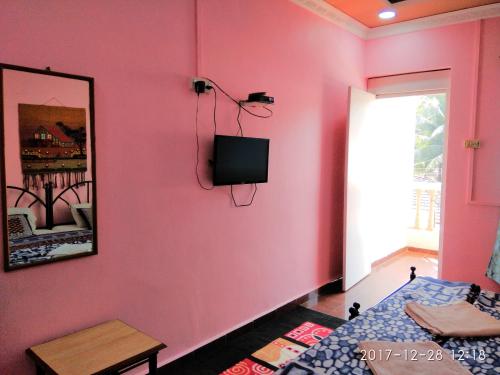 a pink room with a bed and a tv on a wall at Sobitai in Palolem