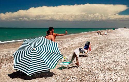 dos personas sentadas en una playa con una sombrilla en Dptos Kandava San Antonio Este en San Antonio Este