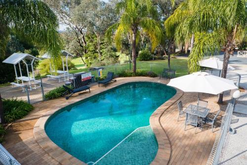 a swimming pool with an umbrella and a table and chairs at Commercial Golf Resort in Albury