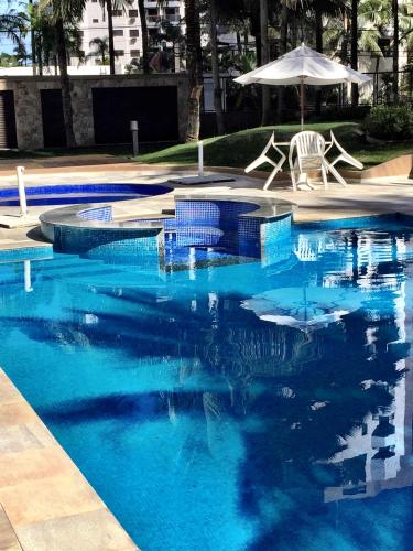 a blue swimming pool with two chairs and an umbrella at Riviera de São Lourenço in Bertioga