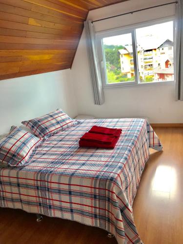 a bedroom with a bed with a plaid blanket and a window at Apartamento no Centro de Gramado in Gramado