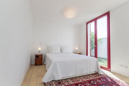 Dormitorio blanco con cama y ventana grande en Quinta da Várzea do Farelo, en Mexilhoeira Grande