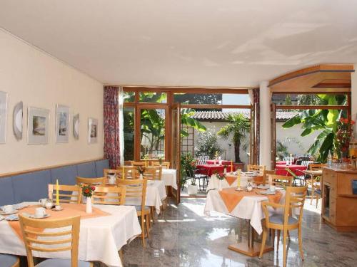 un restaurante con mesas y sillas blancas y ventanas en Appartement Hotel Seerose, en Immenstaad am Bodensee