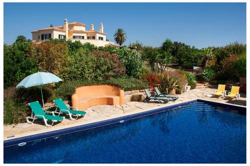 a swimming pool with chairs and an umbrella and a house at Quinta do Sotavento in Moncarapacho